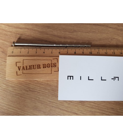 Varão roscado passante M4 de 10cm de comprimento sobre uma mesa, com uma régua de madeira e cartão de visita branco millapoignee