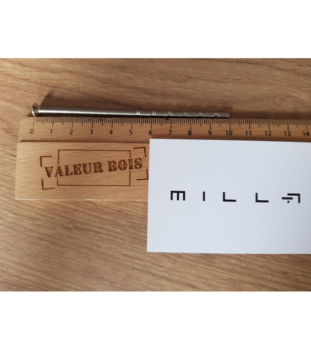 Varão roscado passante M4 de 10cm de comprimento sobre uma mesa, com uma régua de madeira e cartão de visita branco millapoignee