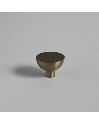 Puxador de móvel redondo em ouro mate LUNA M design pousado numa superfície plana com fundo uniforme