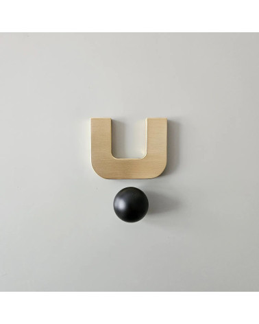 Puxador de móvel ouro polido ISA XS puxador design com uma esfera preta visto de frente sobre uma superfície clara
