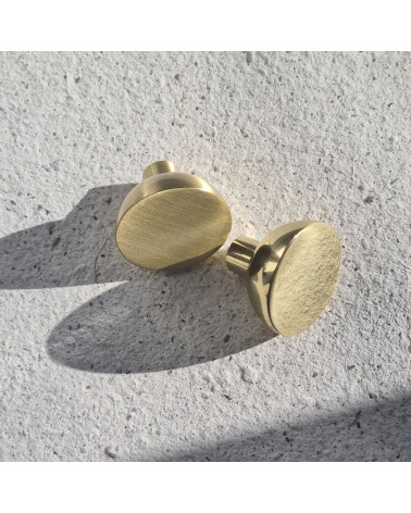 Puxador de móvel dourado polido LUNA M design vista aproximada pousado sobre uma placa texturada