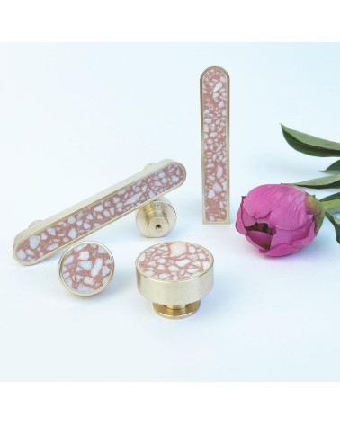 Puxador de móvel em latão e Pink Terrazzo design disposto ao lado de uma flor sobre fundo branco